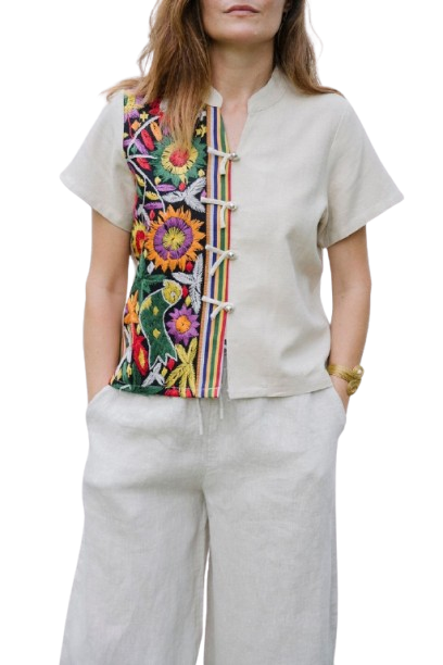 Woman wearing beige linen outfit with colorful floral embroidered panel detail.